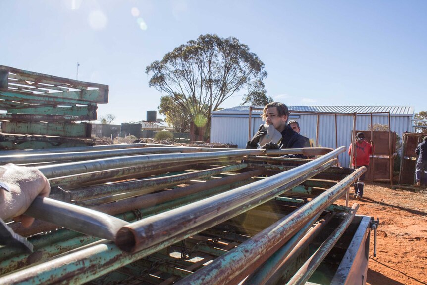 Image of people loading metal stand-up containers onto the back of a ute.