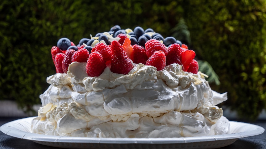 a side view of a tall pavlova, with lashes of cream and summer berries