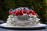 a side view of a tall pavlova, with lashes of cream and summer berries