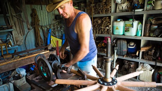 A man builds an old-fashioned wooden-spoked wheel on a workbench.