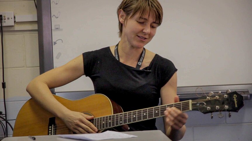 woman in her late 20s early 30s with short hair playing acoustic guitar
