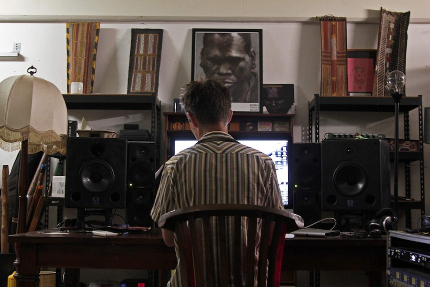 Michael Hohnen sits at a desk in the Skinnyfish Music studio. A portrait of Gurrumul is visible.