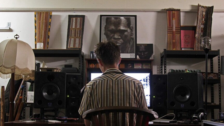 Michael Hohnen sits at a desk in the Skinnyfish Music studio. A portrait of Gurrumul is visible.