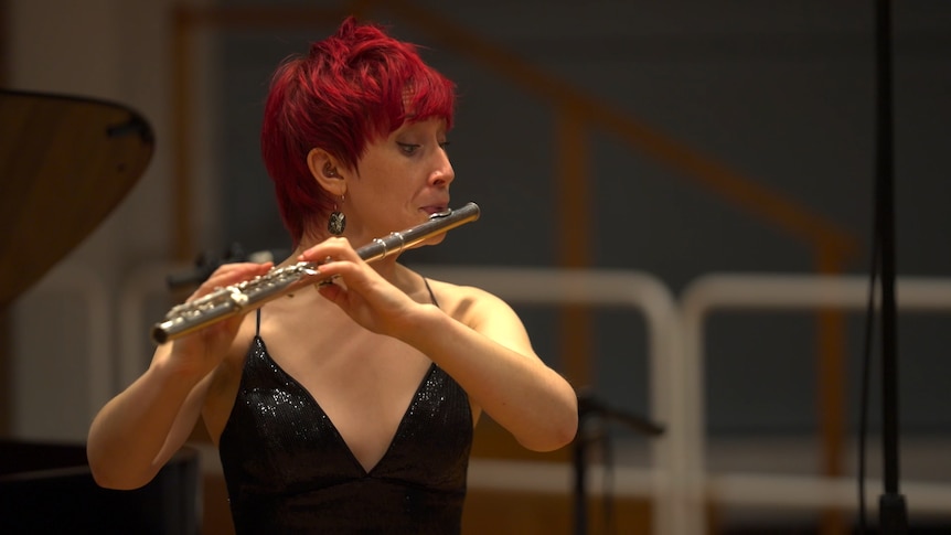 Eliza Shephard plays flute in a sequined top. She has short red hair.