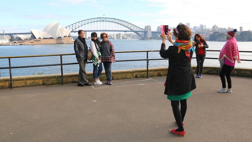 Tourists take photos in front of a view of the Sydney Harbour Bridge.