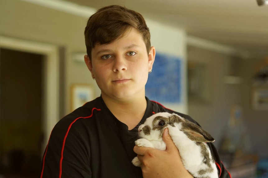 A teenager wearing a black polo shirt holding a rabbit