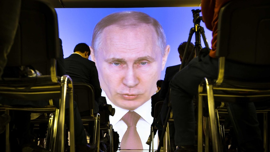 Journalists watch as Russian President Vladimir Putin gives his speech