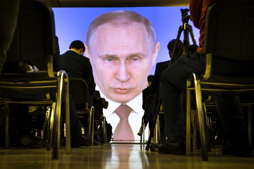 Journalists watch as Russian President Vladimir Putin gives his speech