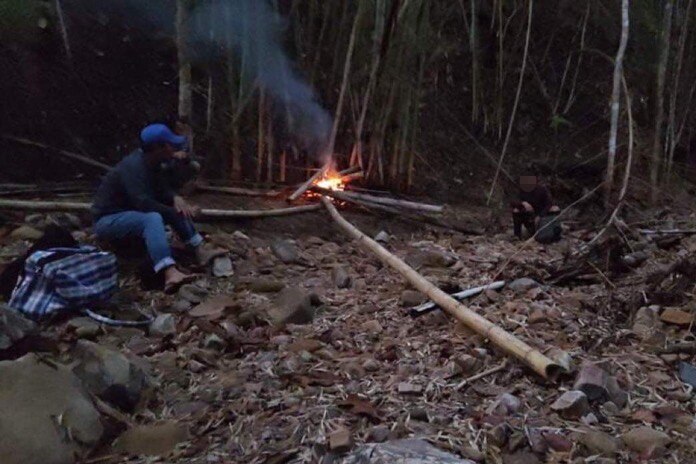 A man sitting by a fire in the jungle.