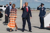 Donald Trump waving while his wife walks next to him on a tarmac