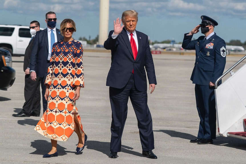 Donald Trump waving while his wife walks next to him on a tarmac