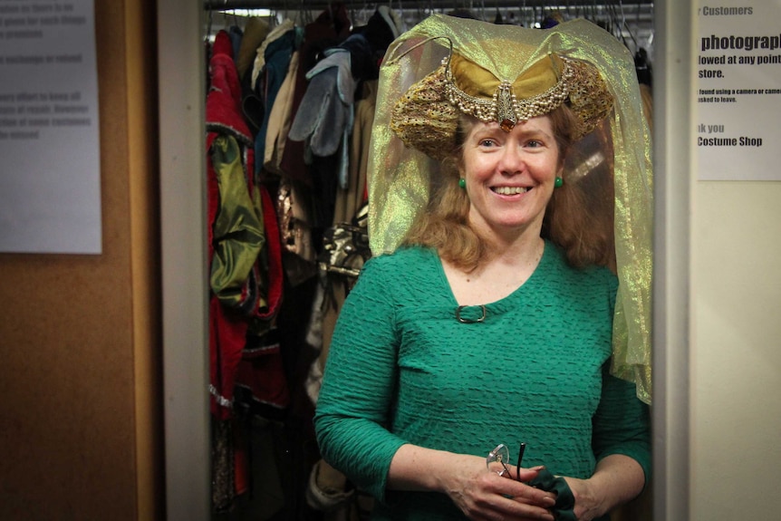 A woman smiling in the mirror, dressed in period costume.