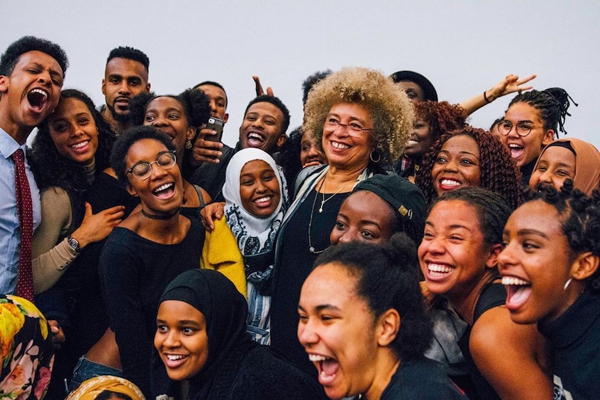 A group of young black people surrounding the activist and academic Angela Davis, everyone is smiling