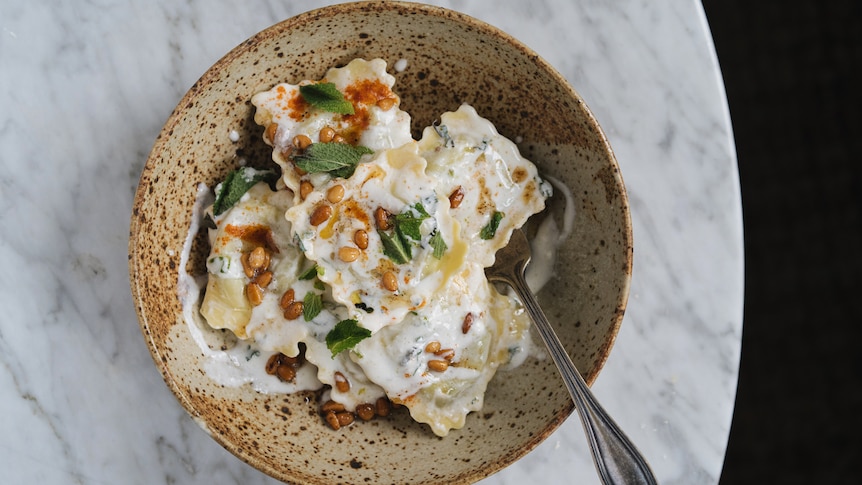 A bowl of ravioli mixed with a mint yoghurt dressing, topped with pine nuts cooked in brown butter, a fast family dinner.