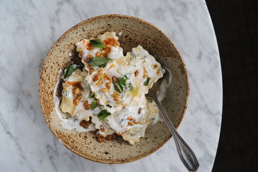 A bowl of ravioli mixed with a mint yoghurt dressing, topped with pine nuts cooked in brown butter, a fast family dinner.