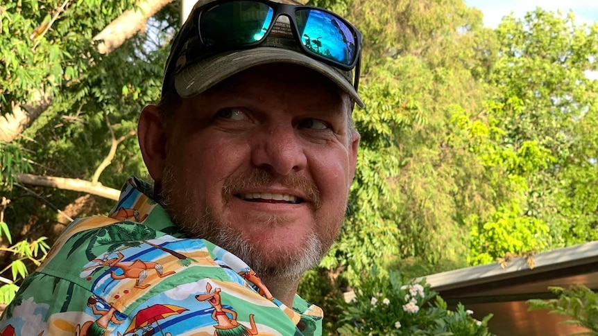 A man in a cap, sunglasses and a multi-coloured shirt.