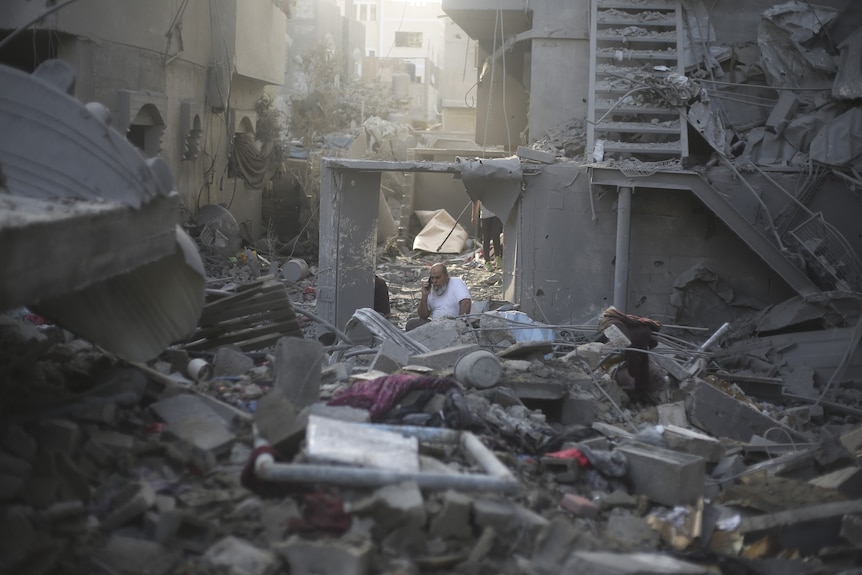 A man sits in rubble on his phone. 