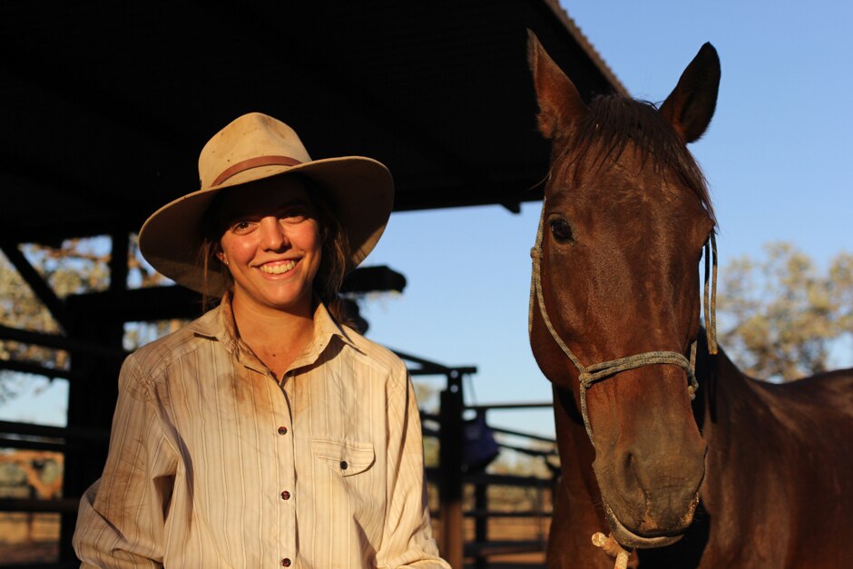 A young woman in a broad-brimmed hat standing beside a brown horse.