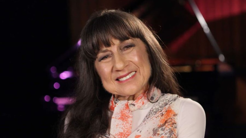 Picture of Judith Durham looking at the camera and smiling she is wearing a white top with orange and red shading.