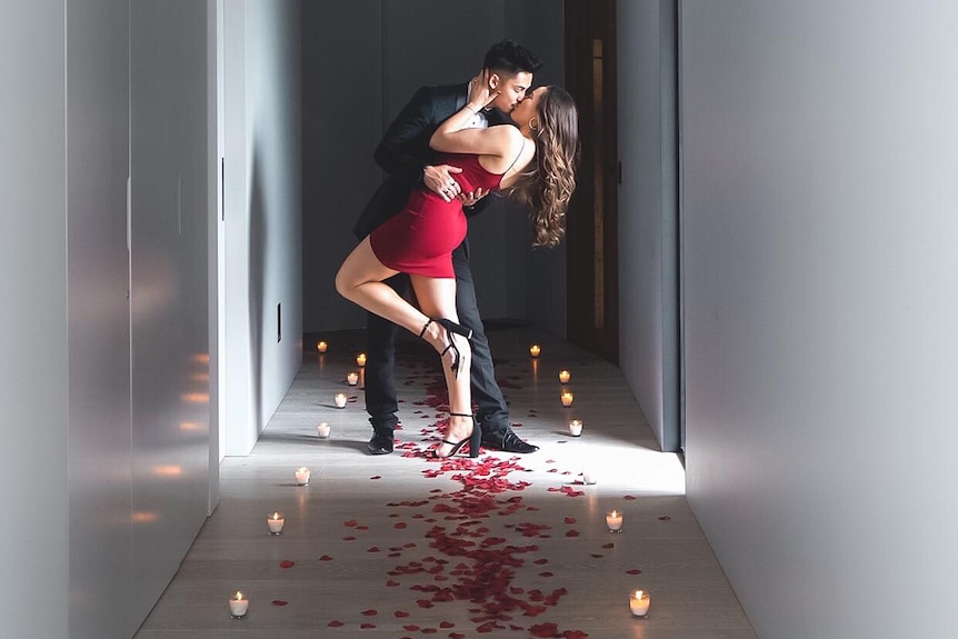 Brandon Jackson and Lara Markham kiss in the hallway, with rose petals on the ground.