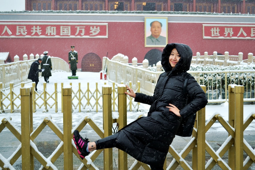 A woman stands in the snow with one leg up sin front of a Chinese building