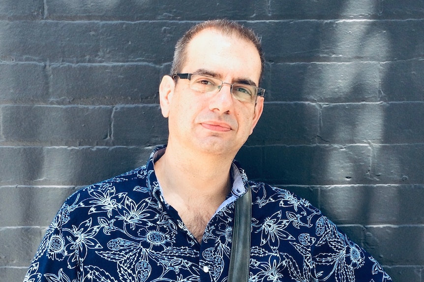 Journalist Fotis Kapetopoulos wearing blue floral-printed shirt and satchel bag.