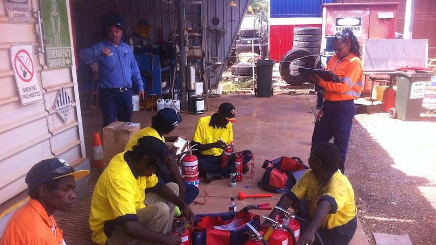Workers sit in a circle on the ground as they receive training