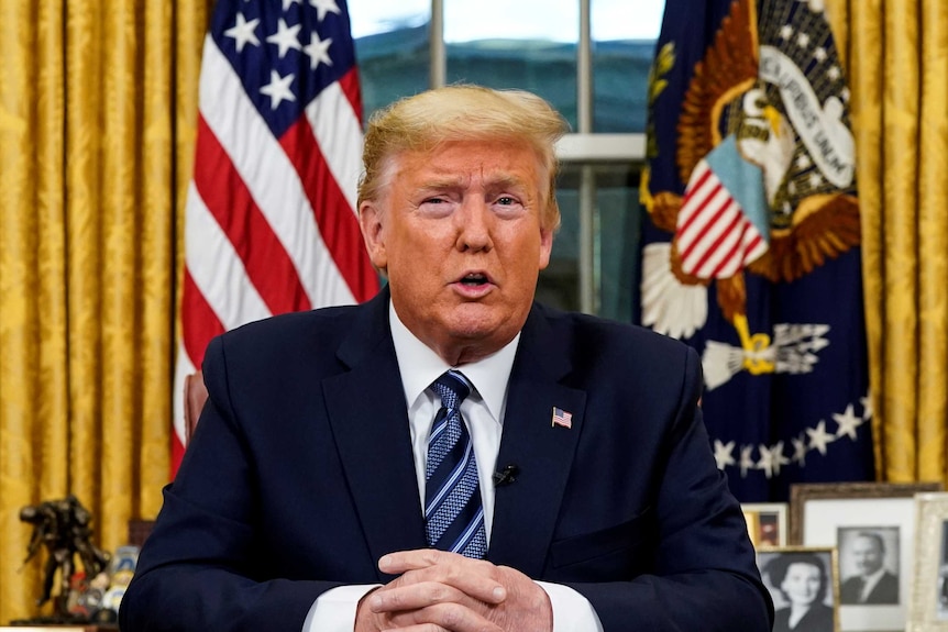 Donald Trump sits behind his desk in front of the American flag as he speaks.