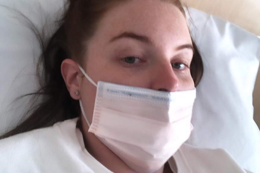 A young woman in a surgical mask lying in a hospital bed