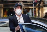 Michael Cohen getting out of a car wearing a face mask and baseball cap.