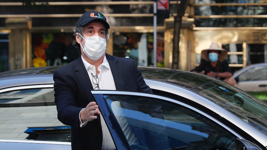 Michael Cohen getting out of a car wearing a face mask and baseball cap.