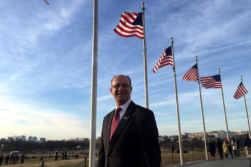 Mike McMullen stands in front of a row of raised US flags