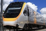 A photo of a Queensland Rail passenger train, with a silver body and yellow doors, at a station on a cloudy day.
