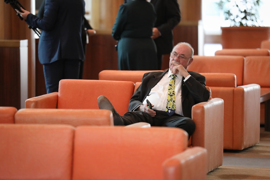 Entsch sits at a couch with one foot resting on a table, looking pensive.