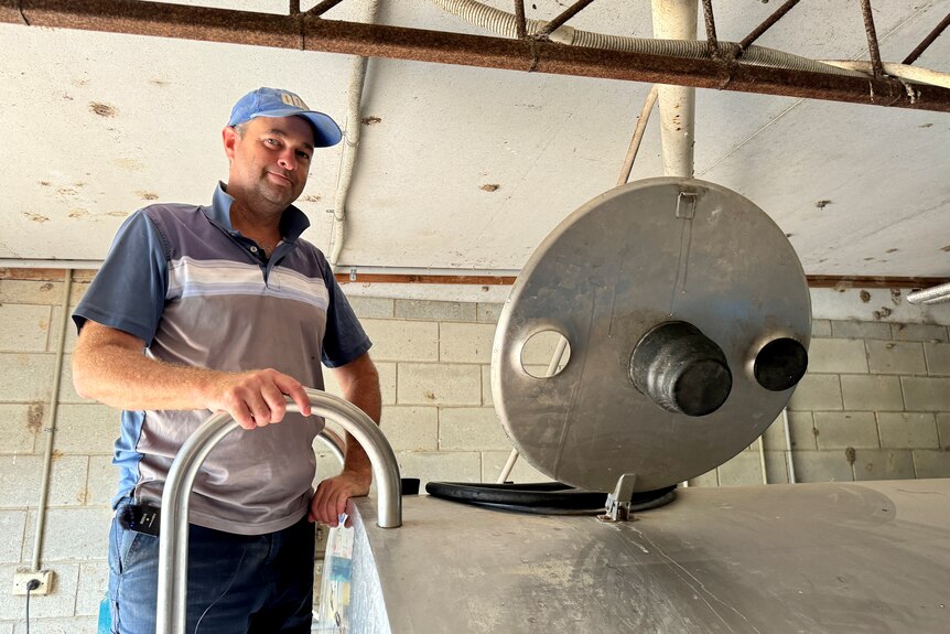 Matthew Trace wearing a blue striped T-Shifrt stands beside a vat of milk.