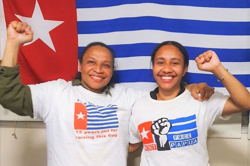 Two woman stand with raised fists in front of a red, white and blue Morning Star Flag 