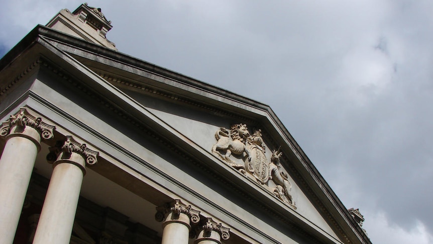 An angled shot looking up at the emblem of Supreme Court (lions and unicorns) with some columns visi