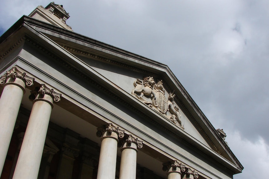 An angled shot looking up at the emblem of Supreme Court (lions and unicorns) with some columns visi