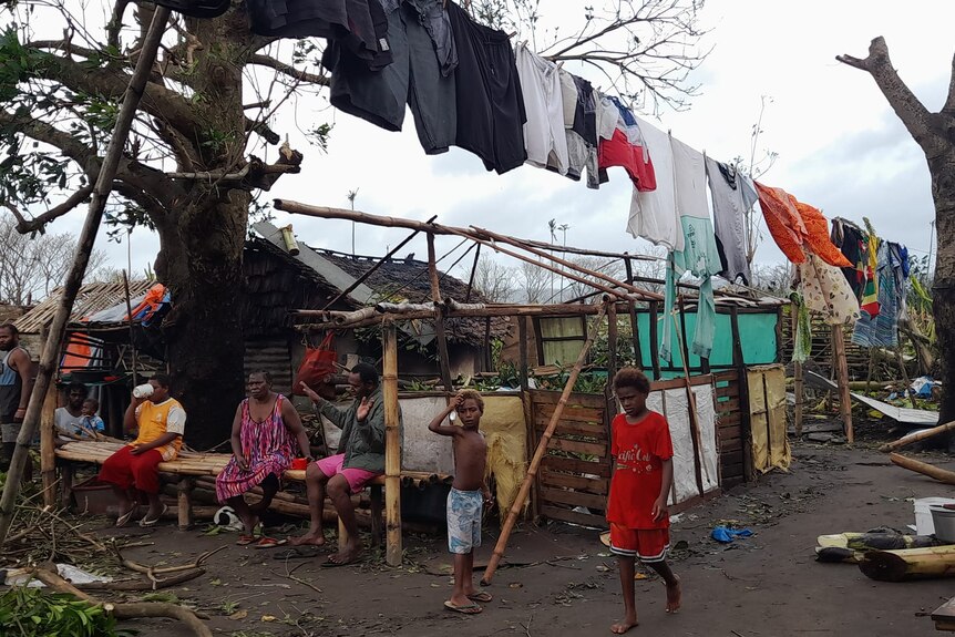 A ni-vanuatu community sit outside underneath hanging washing after cyclone destroys houses