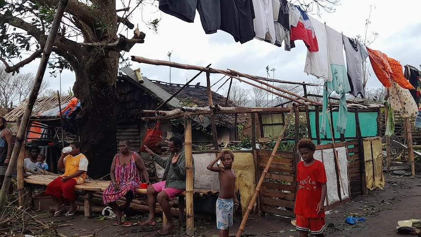 A ni-vanuatu community sit outside underneath hanging washing after cyclone destroys houses