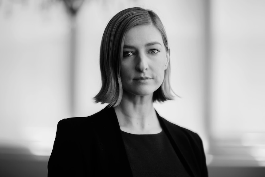 A black and white portrait of a woman with short blonde hair wearing a black suit jacket