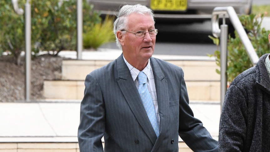 An elderly man in a suit walks slightly behind a man.