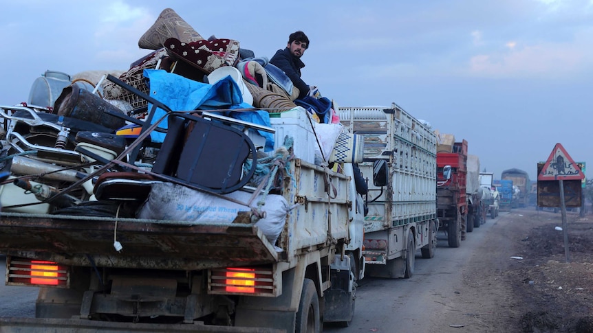 Civilians flee in a long line of trucks loaded with household items.