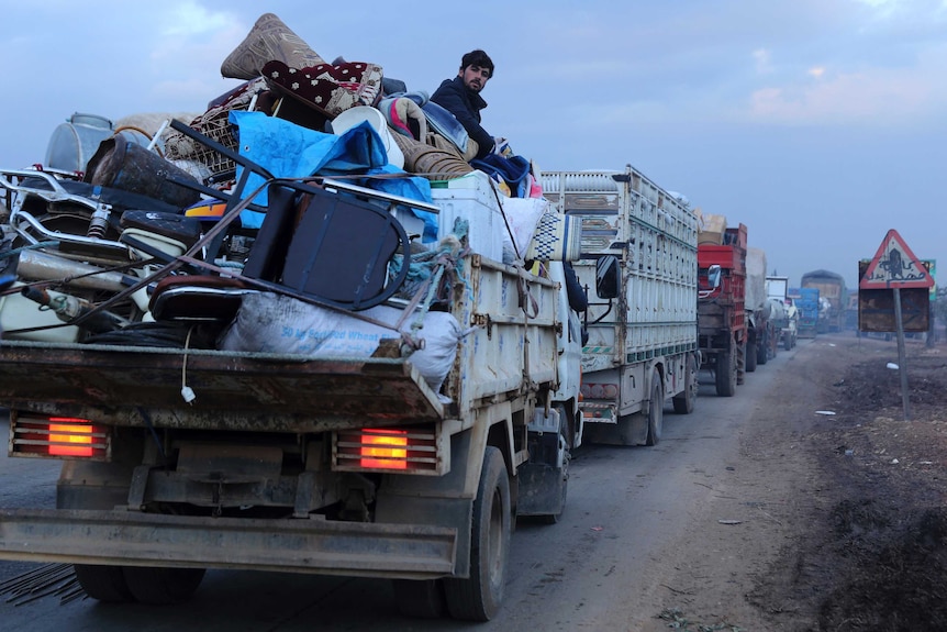 Civilians flee in a long line of trucks loaded with household items.