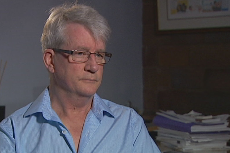 A man with silver hair, wearing a blue shirt and glasses.