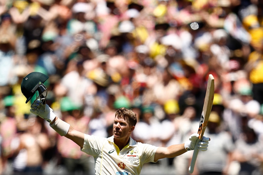 David Warner holds up his bat with the crowd behind him