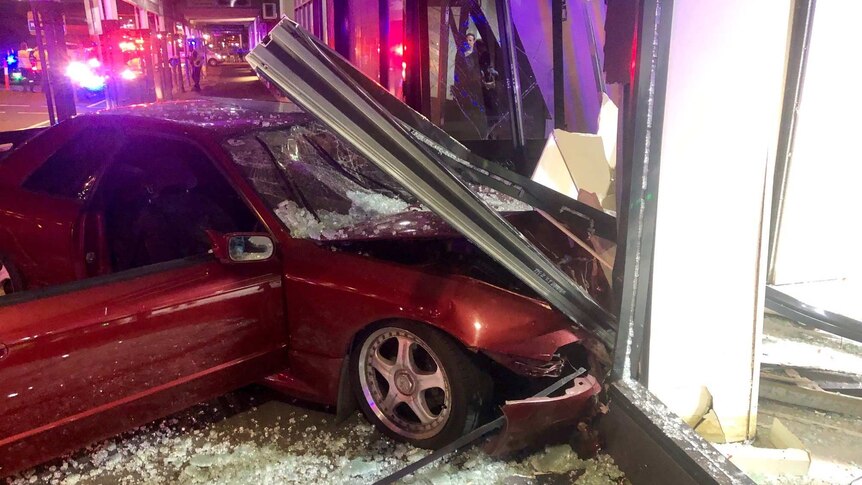 A car covered in glass and debris after crashing into a shop front.