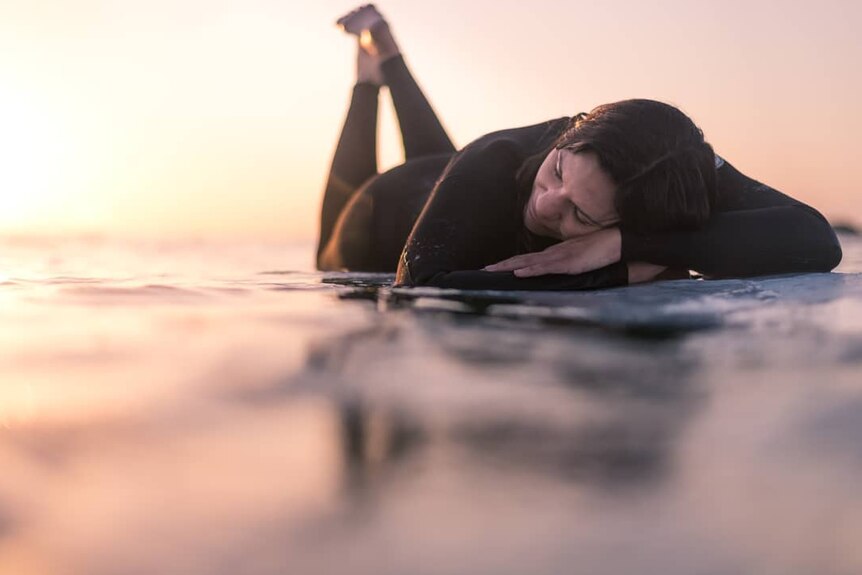 A woman lies on on surfboard
