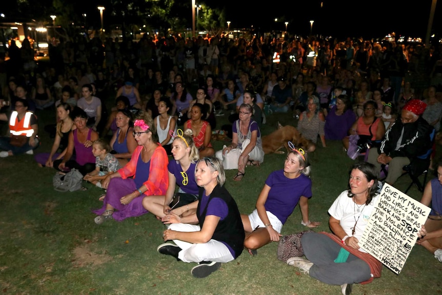 A large crowd of mainly women, some holding signs, sit while listening to speeches