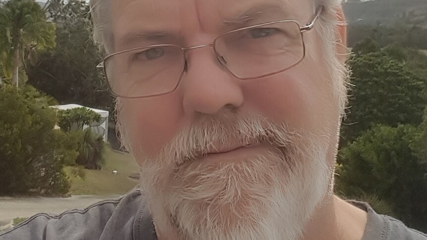 A selfie taken outside of a man with a white beard, short grey hair and glasses.